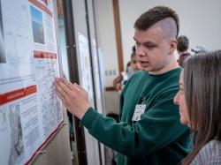 A student discusses his research poster with a faculty member.